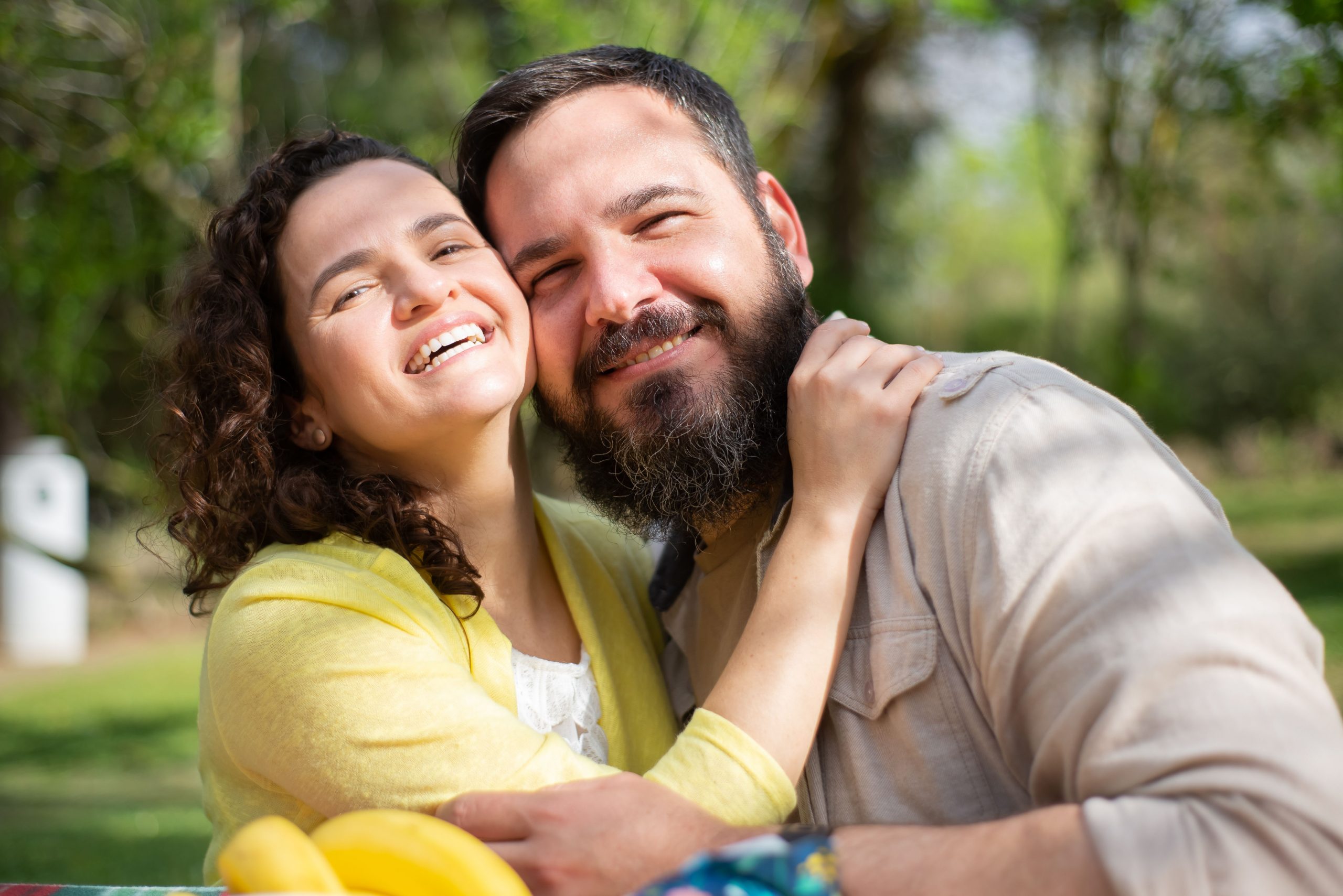 Happy couple smiling and embracing outdoors in a sunlit park, capturing a moment of joy and affection.